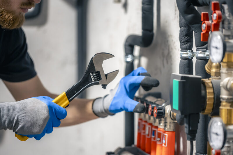 A man installs a heating system in a house and checks the pipes with a wrench. A man installs a heating system in a house and checks the pipes with a wrench.